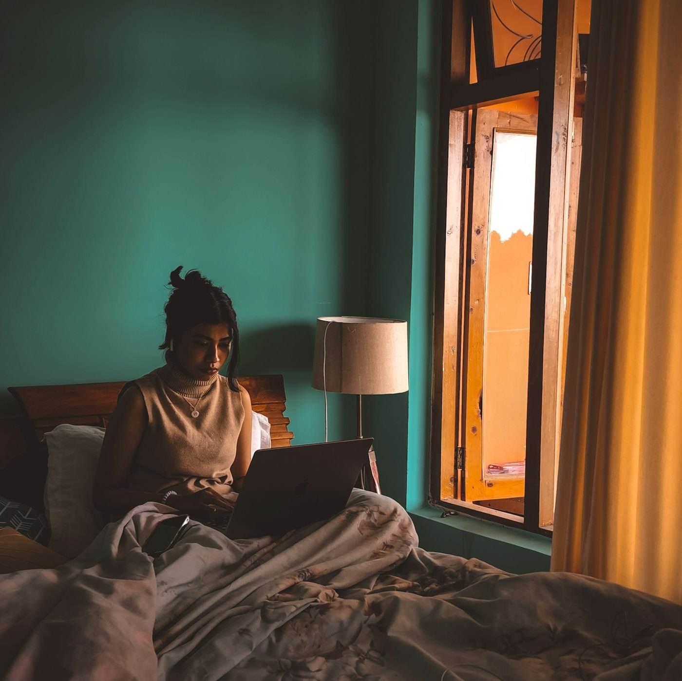 A woman reading on her laptop in bed at dusk