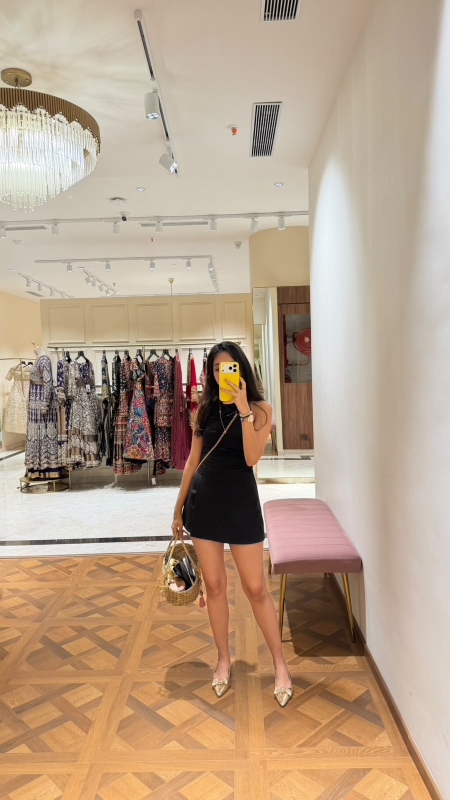 Labdhi Kothari taking a mirror selfie in a black mini dress and gold flats inside a designer wear store
